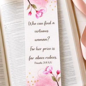 May include: A bookmark featuring the quote "Who can find a virtuous woman? For her price is far above rubies." Pink watercolor design with gold details and floral illustrations. The bookmark rests on an open book.