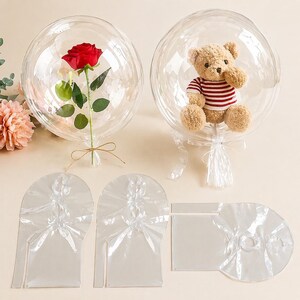 Può includere: Due palloncini rotondi e trasparenti, uno con una rosa rossa e l'altro con un piccolo orsacchiotto con una maglietta a righe rosse e bianche. I palloncini sono legati con nastri. Sono inclusi anche componenti di imballaggio in plastica trasparente.