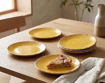 May include: A set of round yellow ceramic plates with a textured, rustic finish and dark speckled edges. One plate holds a single slice of fruit pie, accompanied by a silver metal fork resting on a folded beige linen napkin.