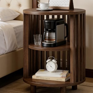 May include: A dark brown, round nightstand with three shelves. The top shelf holds a white teacup and saucer, and a calendar. The middle shelf has a coffee maker and a glass. The bottom shelf has a white alarm clock and books.