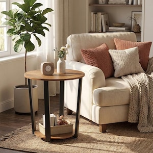 May include: A cozy living room scene featuring a round wooden side table with black legs, a cream-colored sofa with terracotta and cream-colored pillows, and a woven rug. A potted plant and a bookshelf are also visible.