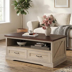 May include: A rectangular coffee table with a dark brown top and light wood base. The table has two drawers and an open shelf. A vase of pink roses sits on top, along with books and a cup. The table is in a living room setting.