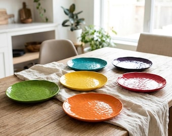 May include: A set of six round ceramic plates in vibrant colors including green, teal, yellow, orange, red, and purple. Each plate features a textured, rippled surface and a glossy finish, arranged on a light-colored fabric runner on a wooden table.