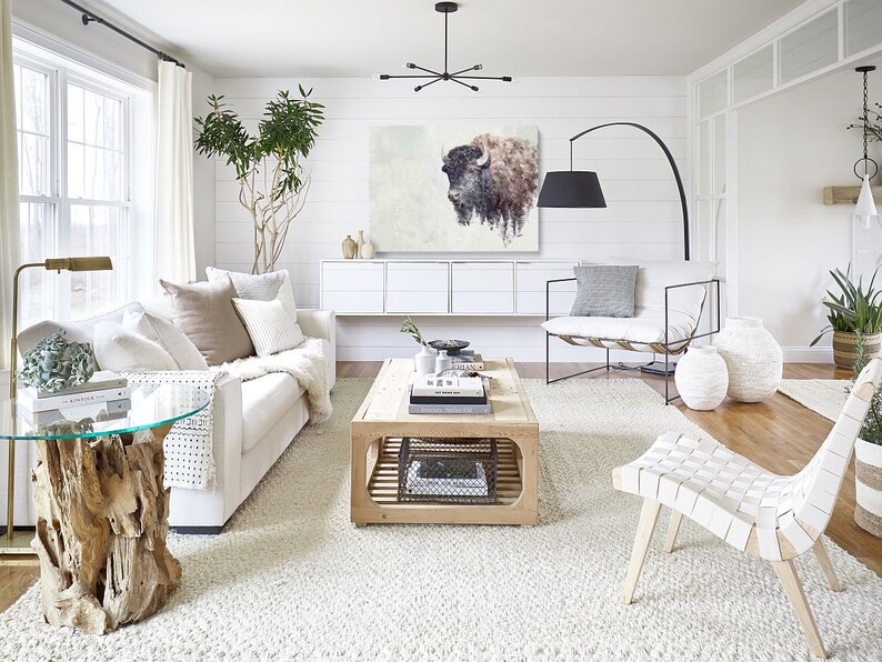 May include: A white living room with a white couch, a white chair, a coffee table, a rug, and a large painting of a buffalo on the wall.