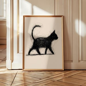 May include: Framed art print featuring a black cat silhouette. The cat is depicted in a walking pose with a curved tail. The artwork is a sketch-like drawing with a gold frame, set against a neutral background.