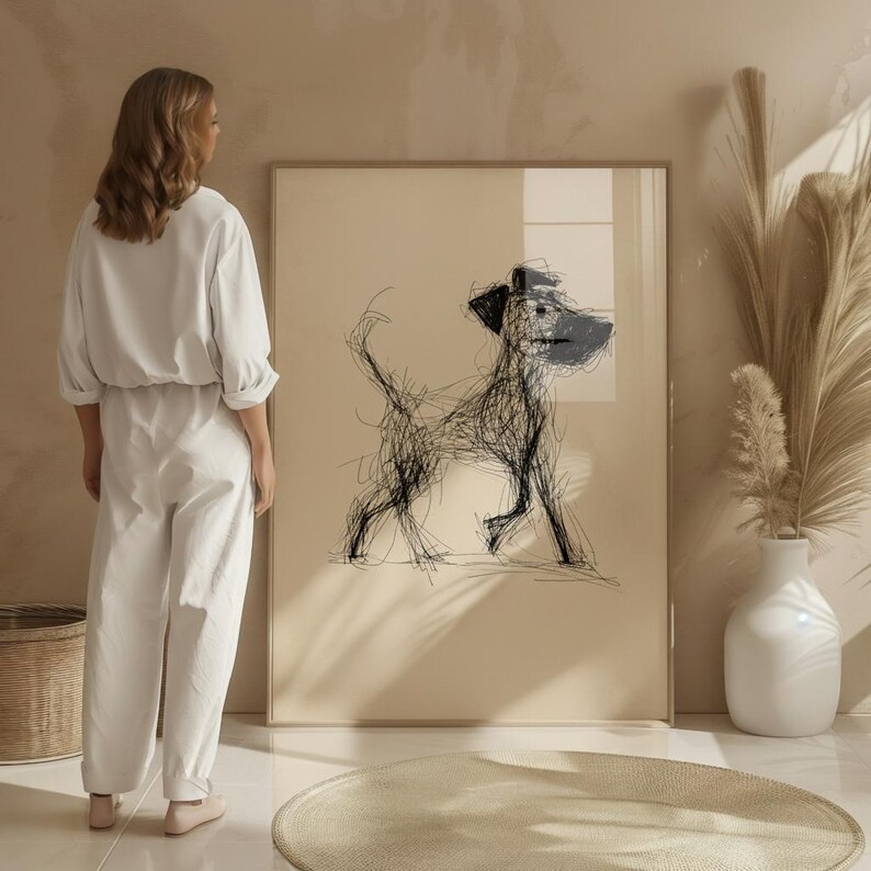 May include: A framed abstract dog sketch in black and blue on a beige background. The artwork is displayed in a room with a woman in white clothing standing nearby. The room has a neutral color palette with a white vase and decorative plants.