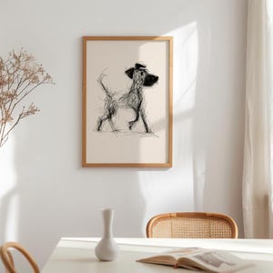 May include: A framed art print featuring a minimalist sketch of a dog in black lines on a cream background. The dog is depicted in a walking pose, with a simple, expressive style. The frame is a light wood color, adding a natural touch to the artwork.