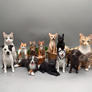Puede incluir: Una colección de figuras de cerámica de gatos y perros de varias razas y colores. Las figuras incluyen un perro blanco y negro, un gato gris y un gato atigrado marrón y blanco. Otras figuras incluyen un gato negro y un perro marrón.