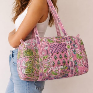 May include: Pink floral print duffel bag with matching handles. The bag features a quilted design with a repeating pattern of flowers and leaves in shades of green, white, and blue. The bag is approximately 30 cm in height and 50 cm in length.