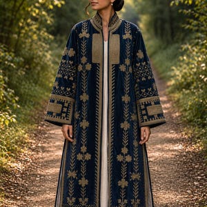 May include: A long, navy blue velvet coat with intricate gold embroidery. The coat features floral and geometric patterns along the sleeves, front, and collar. It is worn over a cream-colored dress, creating a layered look. The coat's design suggests a vintage or bohemian style.