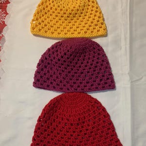 Könnte beinhalten: Drei gehäkelte Hüte in einer Reihe. Der obere Hut ist gelb, der mittlere Hut ist lila und der untere Hut ist rot. Jeder Hut hat ein perforiertes Design.