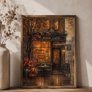 Puede incluir: Una impresión de arte mural enmarcada que representa la fachada de una acogedora cafetería-librería al atardecer. La escena presenta una cálida iluminación interior, follaje otoñal, una pequeña mesa con sillas y un letrero con el texto Coffee, Books, Warmth.