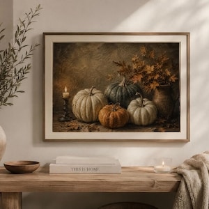 May include: A framed wall art print depicting a still life scene with four pumpkins of varying sizes and colors, including white, orange, and dark green, arranged next to a lit candle in a holder and a vase filled with dried autumn leaves.