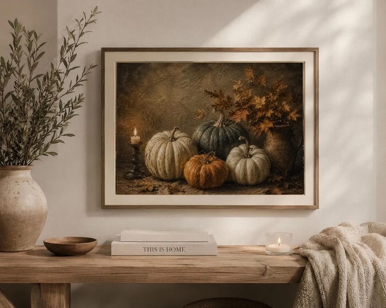 May include: A framed wall art print depicting a still life scene with four pumpkins of varying sizes and colors, including white, orange, and dark green, arranged next to a lit candle in a holder and a vase filled with dried autumn leaves.