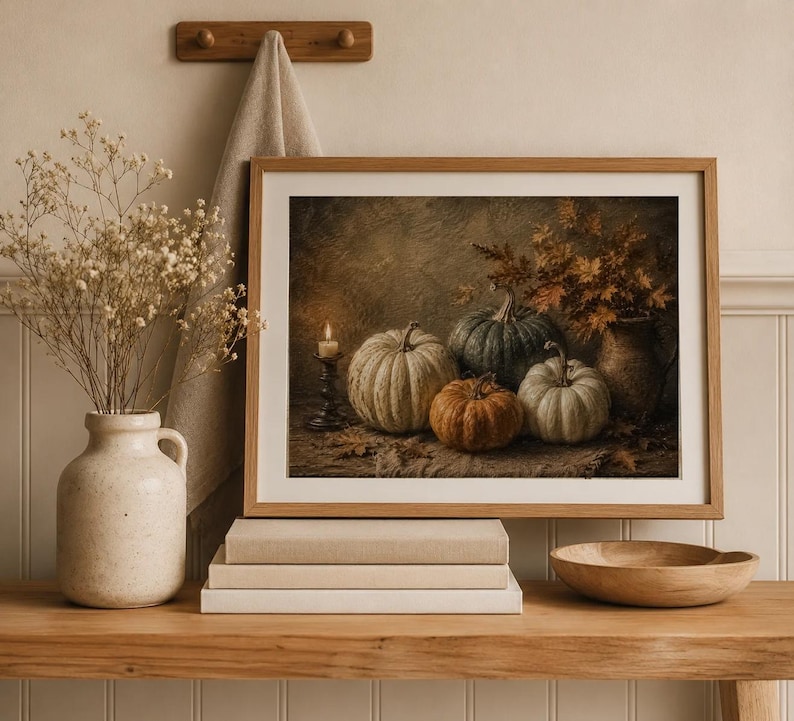 May include: A framed wall art print depicting a still life of four pumpkins in shades of green, white, and orange, a lit candle in a dark holder, and a vase with autumn leaves, all arranged on a textured surface with scattered dried leaves.