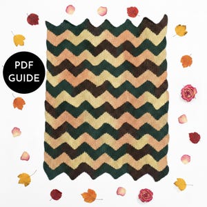May include: A chevron-patterned knitted blanket in shades of green, brown, and beige. The blanket is surrounded by autumn leaves and rose petals. A black circle with the text "PDF GUIDE" is in the image.