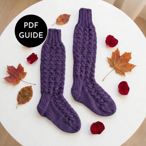 May include: Two knitted purple knee-high socks with a cable knit design. The socks are presented on a white surface, accompanied by autumn leaves and rose petals. A black circle with "PDF GUIDE" text is in the upper left corner.