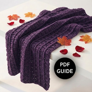 May include: A deep purple, textured crochet blanket draped over a white surface. The blanket is adorned with autumn leaves and rose petals. A black circle with the text "PDF GUIDE" is in the lower right corner.