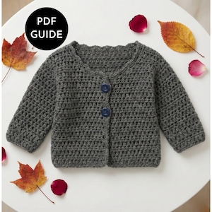 May include: A gray crochet baby cardigan with two blue buttons, displayed on a white surface with autumn leaves and rose petals. The cardigan has long sleeves and a scalloped neckline. A black circle with the text "PDF GUIDE" is in the upper left corner.