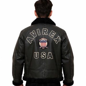 May include: Black leather jacket with a shearling collar and cuffs. The back displays the text "AVIREX USA" and an emblem of the American flag. The jacket has a classic aviator style.