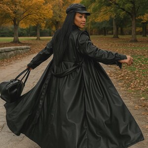 May include: A long, black leather trench coat with a matching belt and a black leather cap. The coat is flowing, and a black handbag is held in the left hand. The background features a park with trees and a walking path.