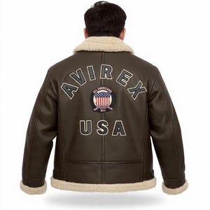 May include: Brown leather jacket with a cream shearling collar and cuffs. The back displays the word "AVIREX" above a circular patch with the American flag and the word "USA" below. A classic aviator-style jacket.