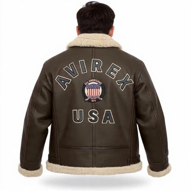May include: Brown leather jacket with a cream shearling collar and cuffs. The back displays the word "AVIREX" above a circular patch with the American flag and the word "USA" below. A classic aviator-style jacket.