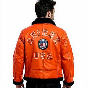 May include: Orange leather jacket with black faux fur collar and cuffs. The back of the jacket features the text "AVIREX USA" with an emblem. A classic bomber jacket style.