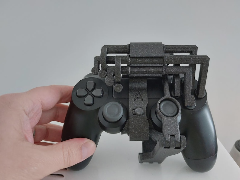 Op de afbeelding: Zwarte gamecontroller met een grijze opzet. De controller heeft een D-pad, knoppen en analoge sticks. De grijze opzet heeft een complex, geometrisch ontwerp en is bevestigd aan de boven- en onderkant van de controller.
