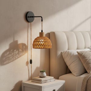 May include: A wall-mounted bedside lamp featuring a woven rattan shade and a wooden base. The lamp has a black metal arm and a tan cord with an on/off switch. The lamp is mounted on a cream wall next to a white bedside table.