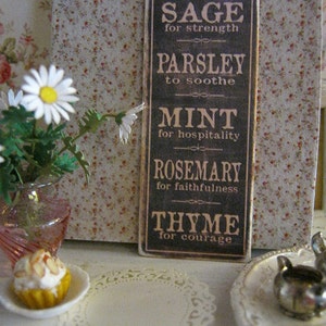 May include: A rectangular sign with a list of herbs and their meanings: Sage for strength, Parsley to soothe, Mint for hospitality, Rosemary for faithfulness, and Thyme for courage. The sign is brown with white text. A cupcake and flowers are also in the image.