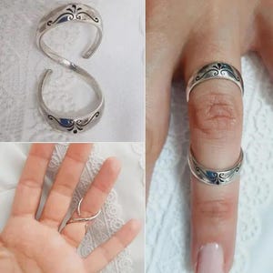May include: Silver-toned ring with an open design, featuring a decorative floral pattern and a dark blue inlay. The ring is shown on a finger and also displayed separately.