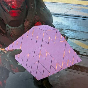 May include: A light purple, geometric, multi-faceted cube object featuring a complex pattern of triangular segments with glowing orange light emanating from the deep crevices between each individual panel, held by a dark, armoured figure.
