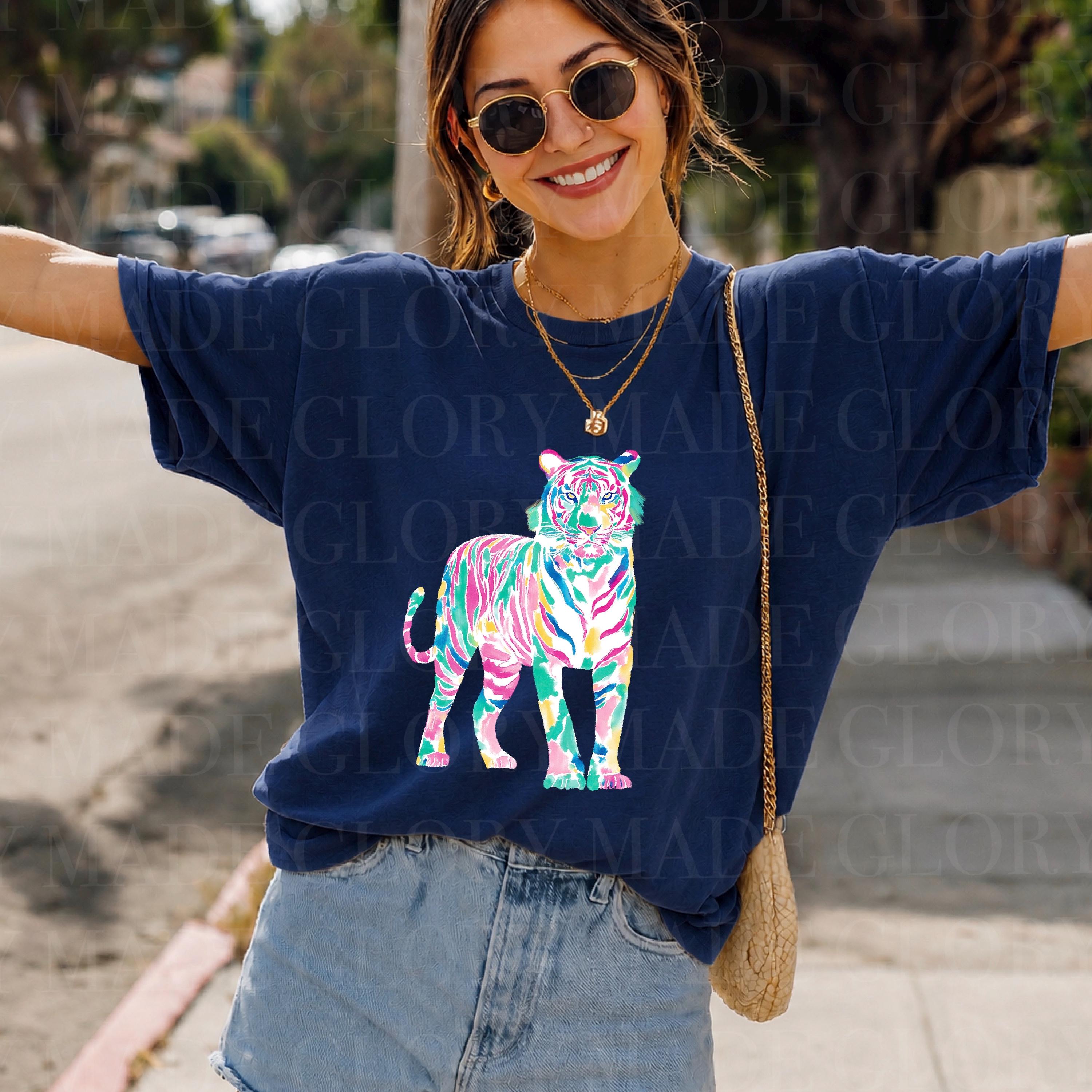 May include: Navy blue t-shirt with a vibrant tiger illustration. The tiger design uses pink, green, blue, and yellow hues. The shirt is a relaxed fit, suitable for casual wear.