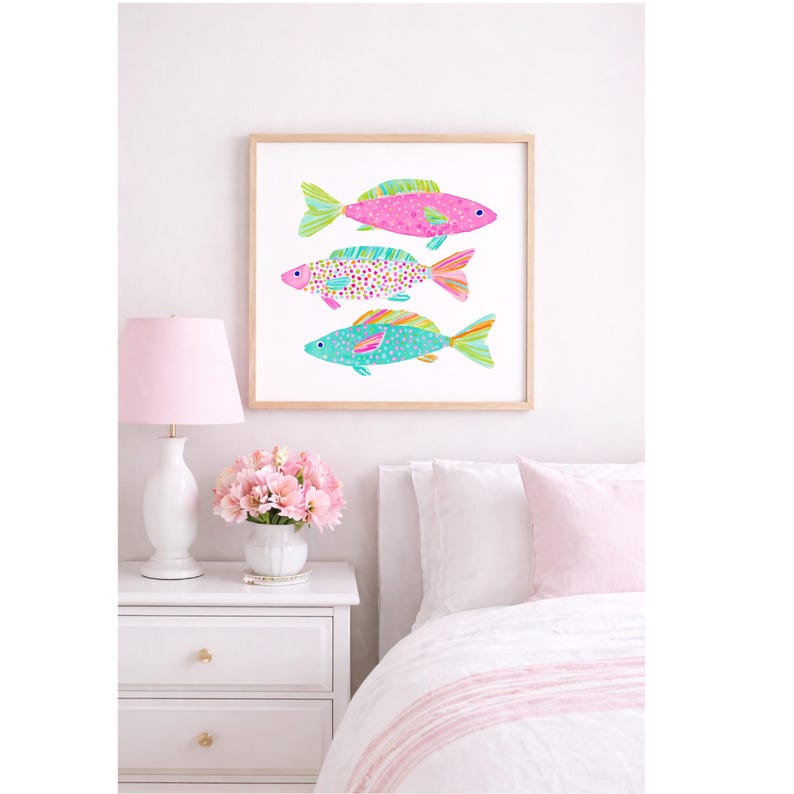 May include: A framed art print featuring three colorful fish illustrations. The fish are pink, turquoise, and patterned with dots and stripes. The artwork is displayed above a white nightstand with a pink lamp and flowers, creating a bright and cheerful bedroom scene.