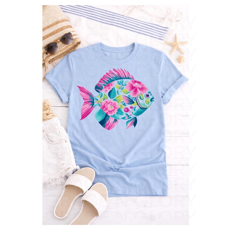 May include: Light blue t-shirt featuring a colorful fish design. The fish is adorned with pink and teal floral patterns. The shirt is styled with white shorts, sandals, a straw bag, and sunglasses, suggesting a summer theme.