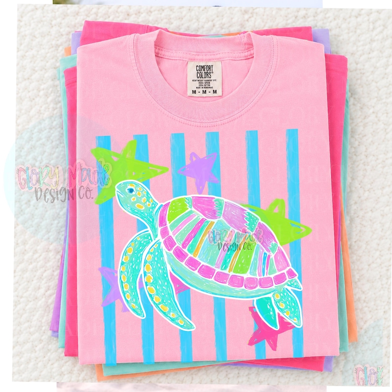 May include: A light pink short-sleeve t-shirt featuring a graphic of a sea turtle with a multi-colored shell in shades of pink, green, and blue. The design includes vertical blue stripes and several star shapes in lime green and pink.