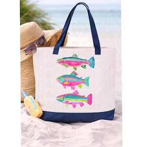 May include: White canvas tote bag with a navy blue base and handles. The bag features three colorful fish illustrations in shades of pink, blue, and green. A straw hat, sunglasses, and sunscreen are in the background.