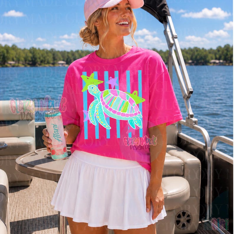May include: A bright pink short-sleeve t-shirt featuring a graphic of a sea turtle with colorful stripes and patterns, accented by light blue vertical stripes and small stars. The shirt is paired with a plain white pleated athletic skirt.