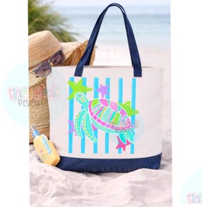May include: A white tote bag with dark blue handles and a dark blue base. The front features a colorful sea turtle graphic in shades of pink, green, and blue, set against vertical light blue stripes and accented with small pink and green stars.