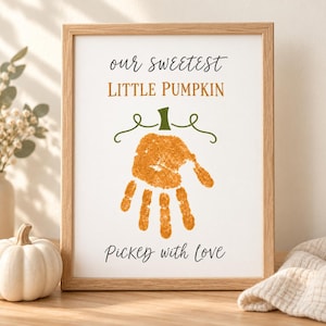 Op de afbeelding: Een ingelijste print met de tekst "our sweetest LITTLE PUMPKIN" in zwart en oranje, een centrale oranje handafdruk in de vorm van een pompoen met een groene steel en ranken, en de tekst "Picked with love" in het zwart onderaan.