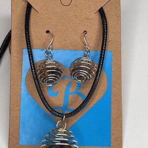 May include: A jewelry set featuring a necklace and earrings. The necklace has a pendant with a silver wire cage holding a brown stone. The earrings have a similar design. The set is displayed on a brown card with a blue heart-shaped design.