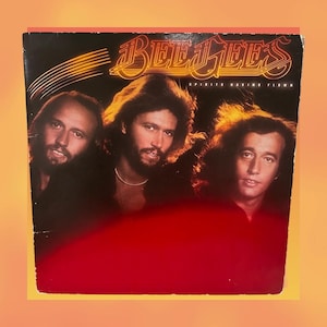 May include: Album cover for the Bee Gees' "Spirits Having Flown." The album art features three men with long hair, set against a black background with the band's name in gold lettering. A red gradient fills the bottom half.