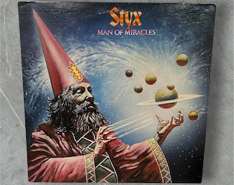 May include: Album cover for Styx's "Man of Miracles." The artwork features a wizard in a red robe and hat, with a long white beard, conjuring planets and orbs against a starry background. The band's name and album title are in orange.