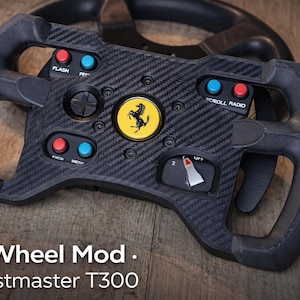 Puede incluir: Un GT Wheel Mod negro para Thrustmaster T300. El volante presenta un diseño de fibra de carbono con botones rojos y azules, un panel direccional y un logotipo de Ferrari. El volante tiene un indicador y está sobre un fondo de madera.