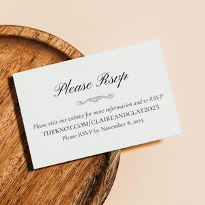 May include: A white RSVP card with elegant script, resting on a wooden tray. The card reads "Please RSVP" and includes website and RSVP deadline information. The background is a soft peach color.
