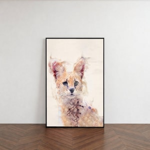 Puede incluir: Pintura a la acuarela de un serval con grandes orejas y pelaje manchado. La obra de arte está enmarcada en un marco rectangular negro y se apoya contra una pared blanca. El pelaje del gato es una mezcla de colores beige, marrón y crema.