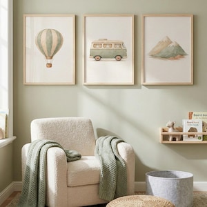 Peut inclure: Trois impressions encadrées à l'aquarelle représentant une montgolfière, un van vintage et des montagnes. Un fauteuil crème avec une couverture verte est devant les impressions. Un pouf tressé et un panier en feutre gris sont au sol.