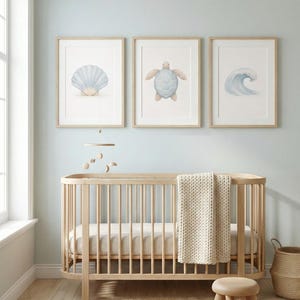 May include: Three framed watercolour prints of a seashell, sea turtle, and wave hang above a wooden cot. The cot has a cream-coloured blanket draped over the side. A small wooden stool and a woven basket sit on a jute rug.