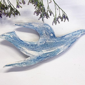 May include: A blue and white ceramic bird wall hanging with a marbled glaze. The bird is in flight with its wings spread out.
